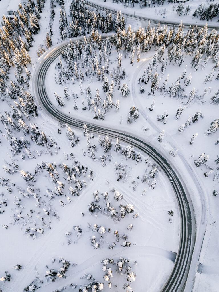 Aerial view of Curvy Windy Road in snow covered forest in Winter Finland, Lapland, top view.